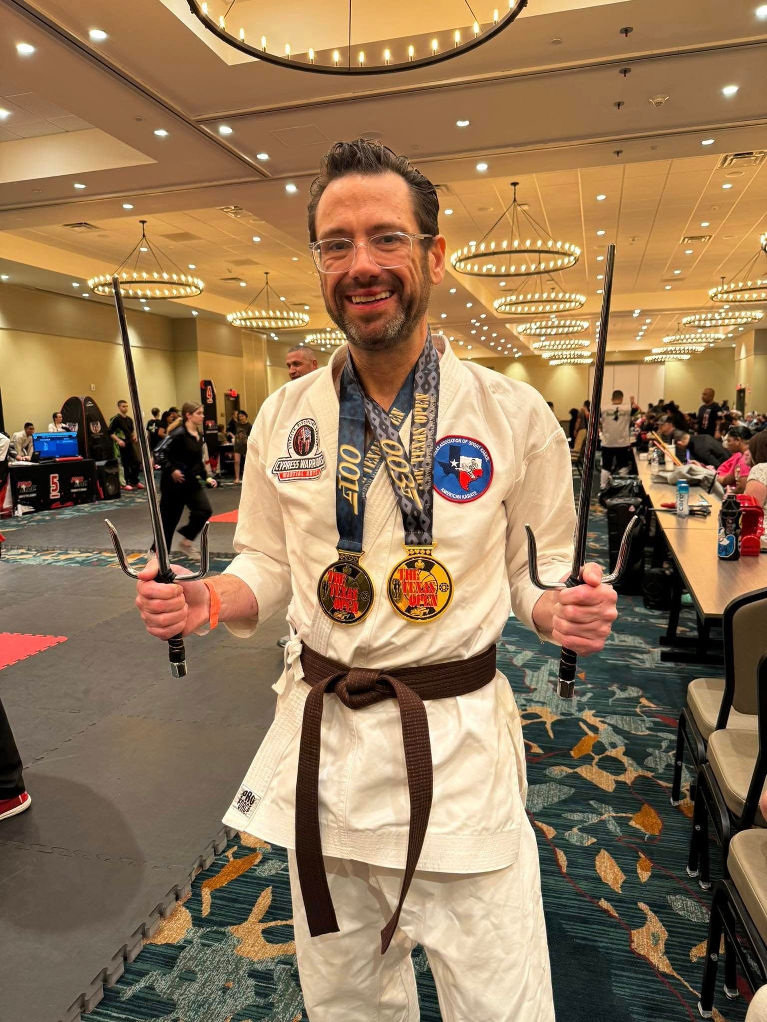 Bob Huff in a white karate uniform holding sai and wearing tournament medals.